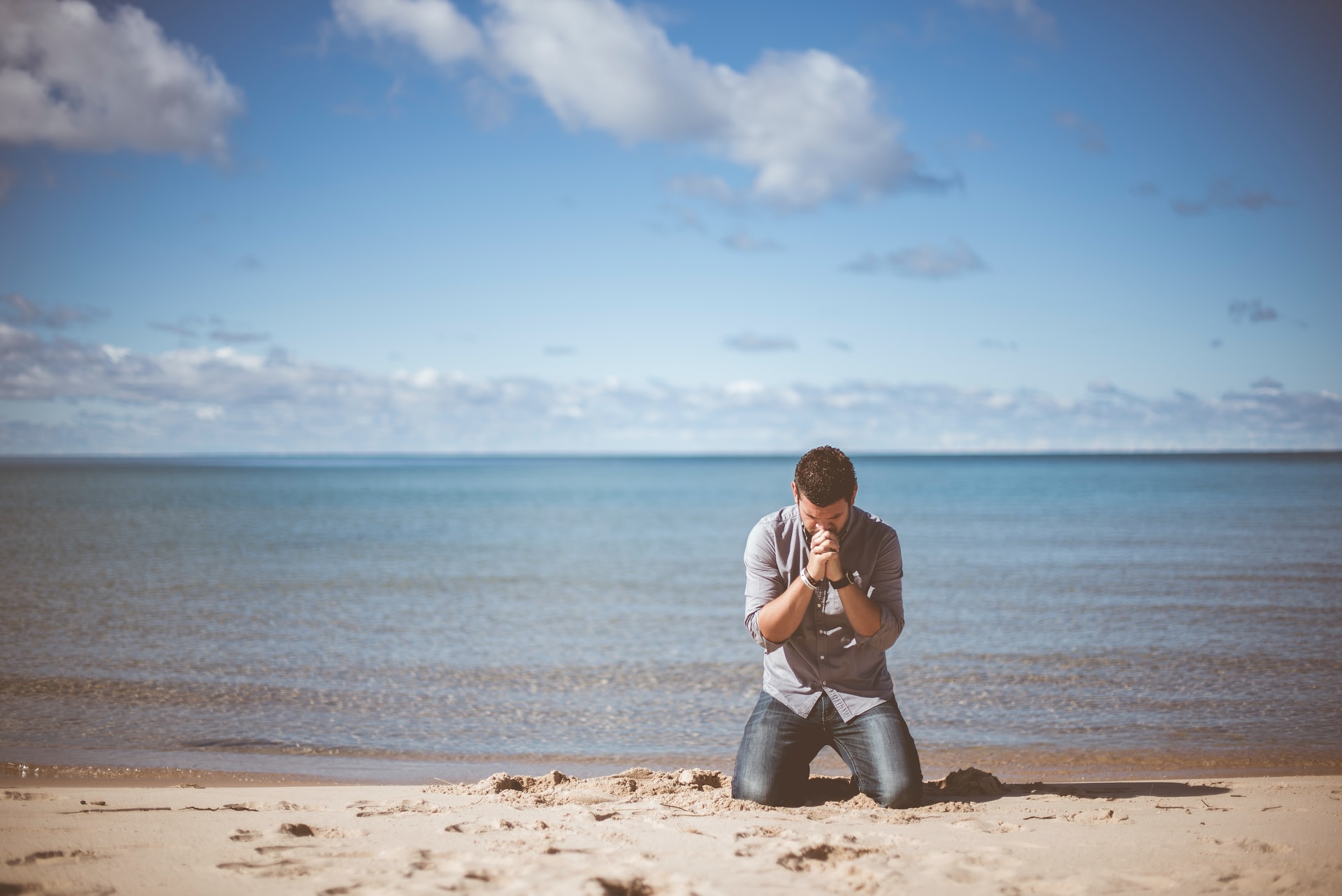man kneeling in prayer at the beach